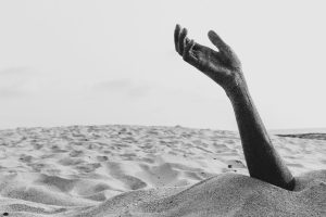 A dramatic black and white image of a hand buried in the sand on Alappuzha beach, Kerala.