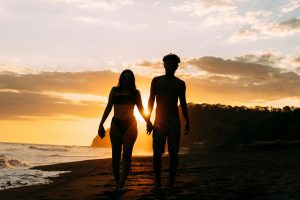 Silhouette of couple holding hands at sunset on a tropical beach.
