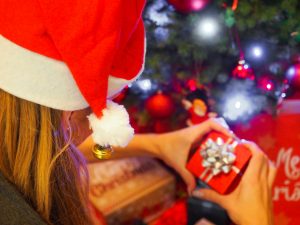 Woman in a Santa hat wrapping presents under a decorated Christmas tree.